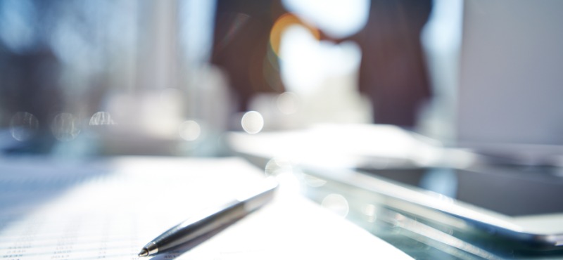 paper on a table with a pen and two lawyers in the distance with a blurry background
