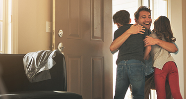 Man entering home and hugging two children in doorway