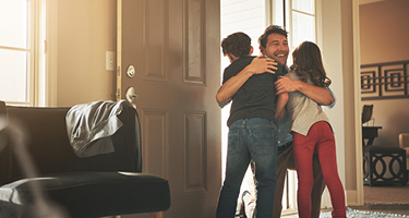Man entering home and hugging two children in doorway