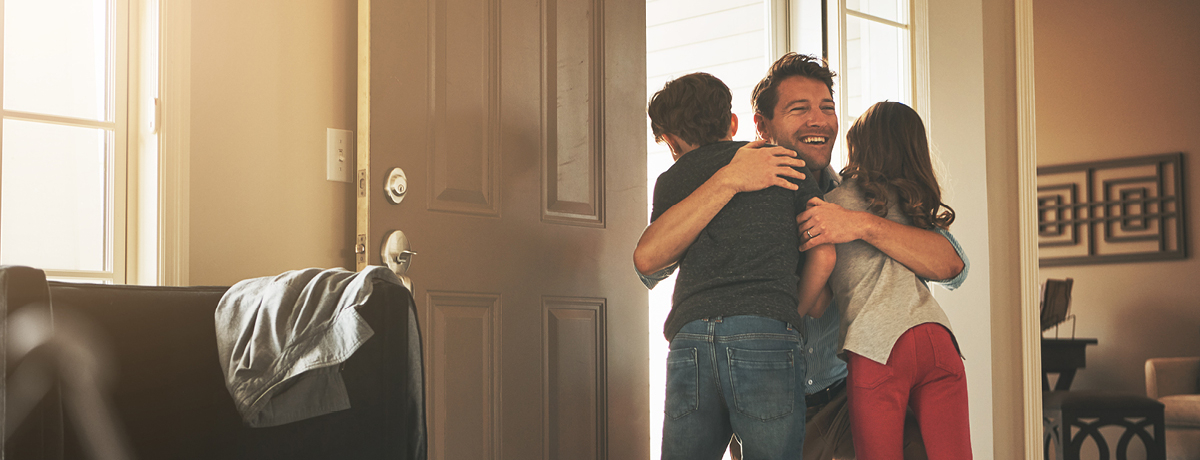 Man entering home and hugging two children in doorway