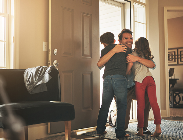 Man entering home and hugging two children in doorway