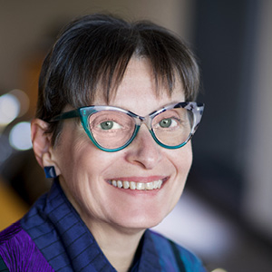 Woman with dark hair and glasses smiling for headshot