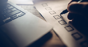 Laptop corner and hand checking box on paper