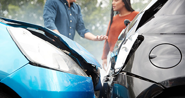 Blue car and grey car crashed into each toher with woman and man standing beside them talking