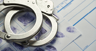 Silver handcuffs laying on finger printed papers