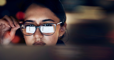 A woman with a laptop screen reflected in her glasses