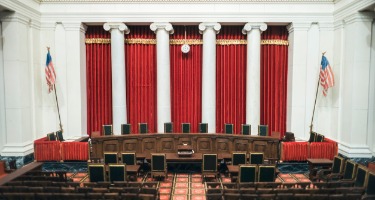 Inside of the Supreme Court building with billowing red curtains and American flags 