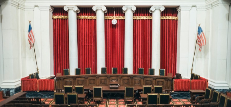 Inside of the Supreme Court building with billowing red curtains and American flags 