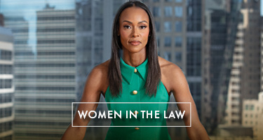 Lawyer in green dress stands with hands on table and cityscape in background 