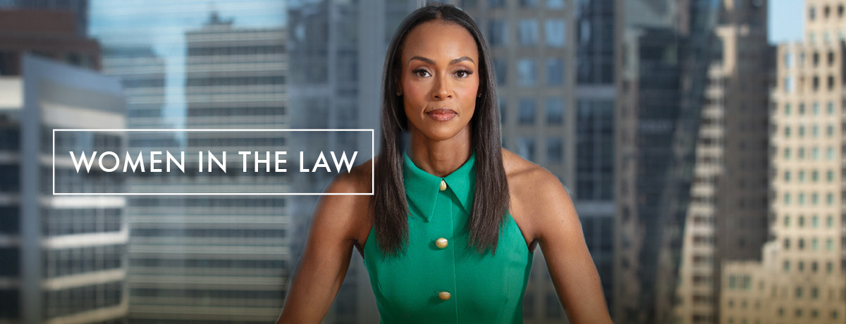 Lawyer in green dress stands with hands on table and cityscape in background 