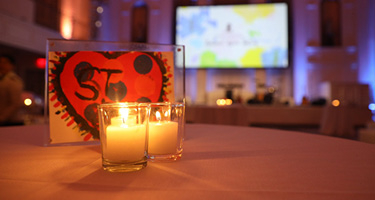 Two candles on table in front of framed child's artwork and large screen at event