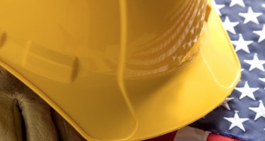 A yellow construction helmet and worker gloves on the American Flag