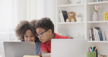 Two children seated, using laptops