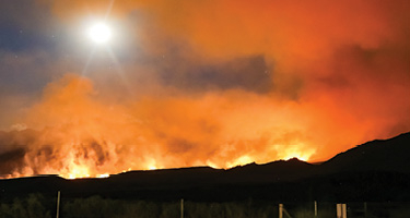 Mountain range with glow of wildfires behind it