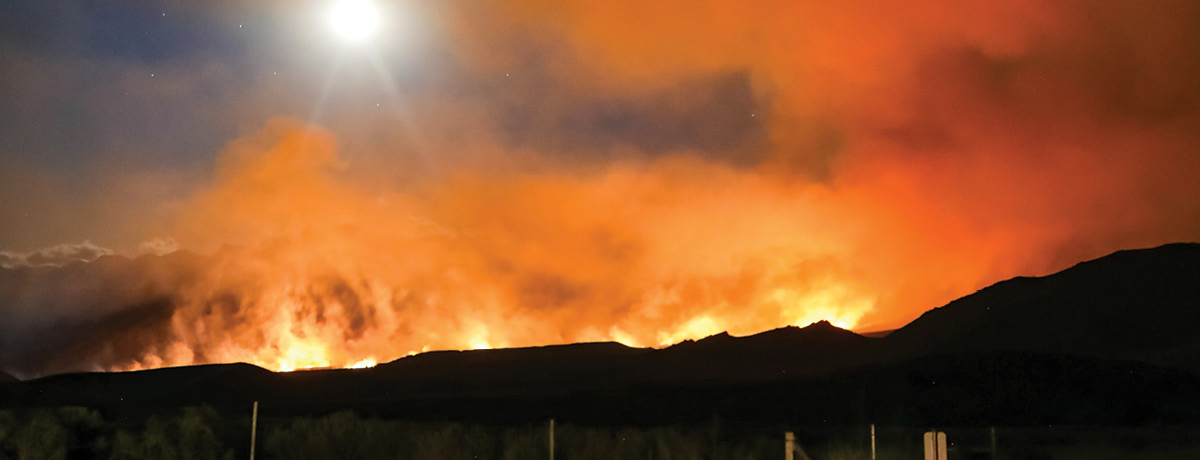 Mountain range with glow of wildfires behind it