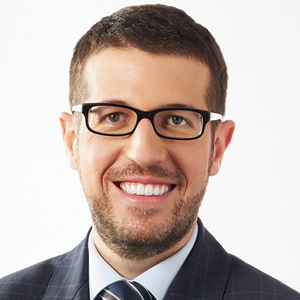 Man with dark hair and glasses in grey suit