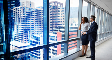 Two corporate employees standing near window with cityscape