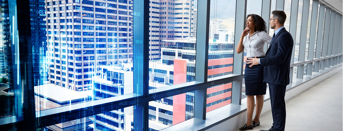 Two corporate employees standing near window with cityscape