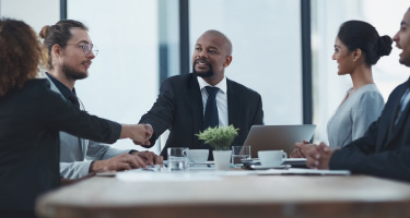 Professional men and women sitting around a table shaking hands and making business deals