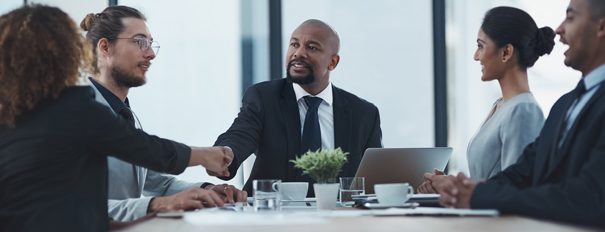 Professional men and women sitting around a table shaking hands and making business deals