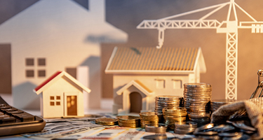 Paper houses and money sitting amongst coins and money