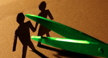 Paper man and woman hold hands next to green scissors trying to cause a separation