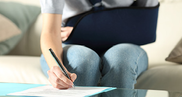 close up of a woman in an arm sling signing a paper
