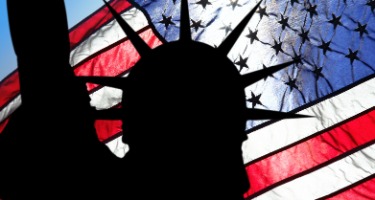 Silhouette of the Statue of Liberty with the American flag flying high in the background 