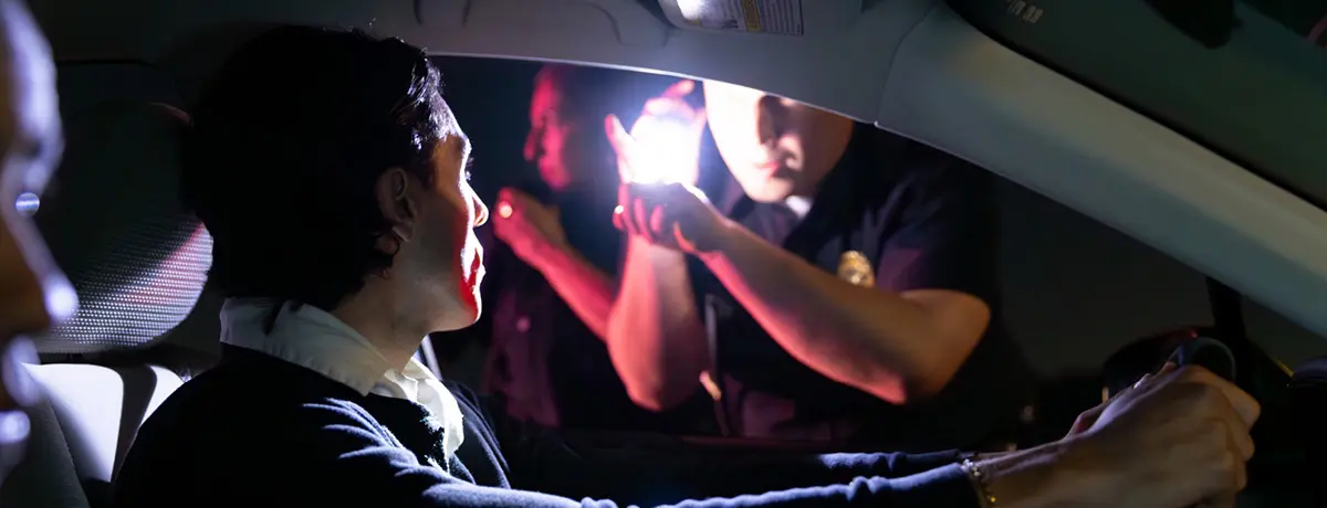 Driver during nighttime police traffic stop with officer's flashlight shining through car window