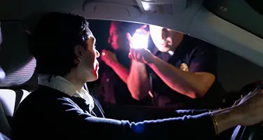Driver during nighttime police traffic stop with officer's flashlight shining through car window
