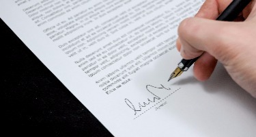 Close-up of a hand holding a pen and signing a formal document.