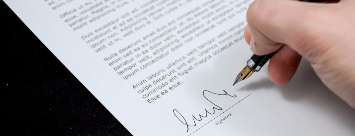 Close-up of a hand holding a pen and signing a formal document.