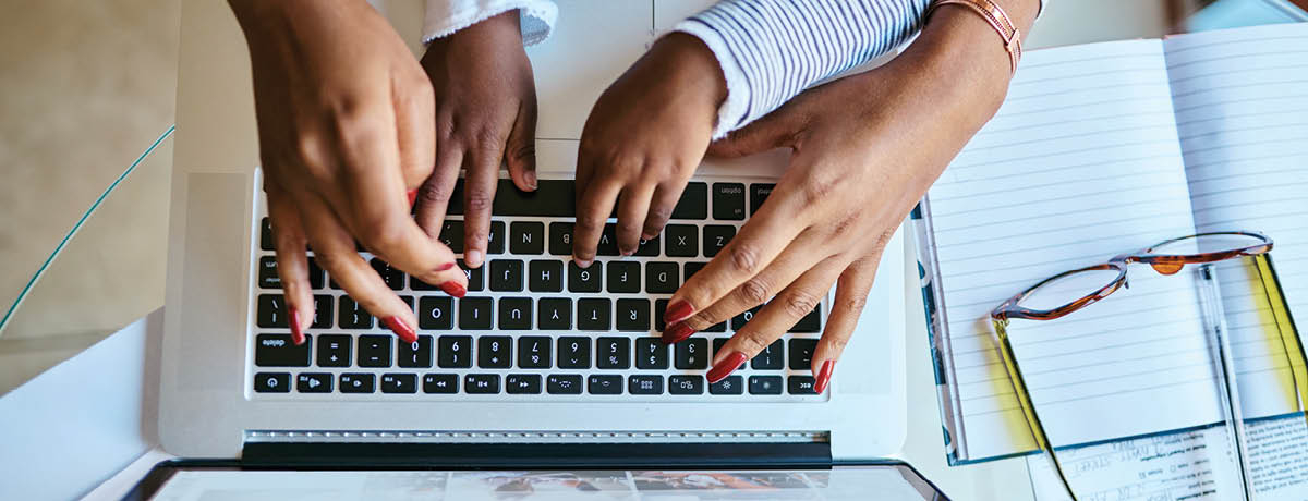 Two sets of hands typing on a laptop
