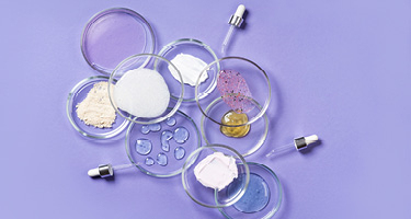 Petri dishes and tubes of makeup and cream on lavender background
