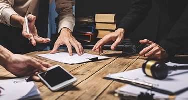 Hands joined around a table with phone, paper, pen and glasses