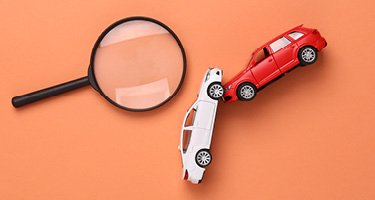 Red and white toy car colliding by magnifying glass on orange background