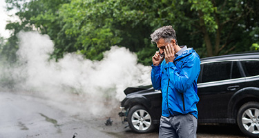 Man in blue jacket standing in front of smoking car