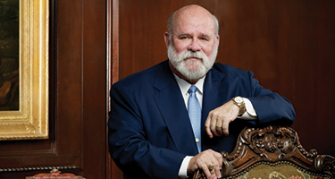 Man in suit stands with hands on chair