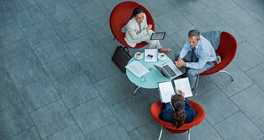 One male and two females working together at table with computer and notebooks