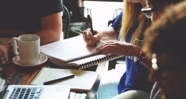 Group of professionals gathered around a table with coffee cups, notebooks and laptop.