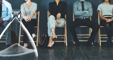 Group of people sitting in wooden chairs watching a sand timer run out