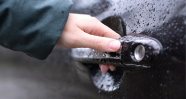 Man opening his car door with his hand wearing a rain jacket