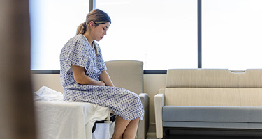 Woman in hospital gown sits on bed