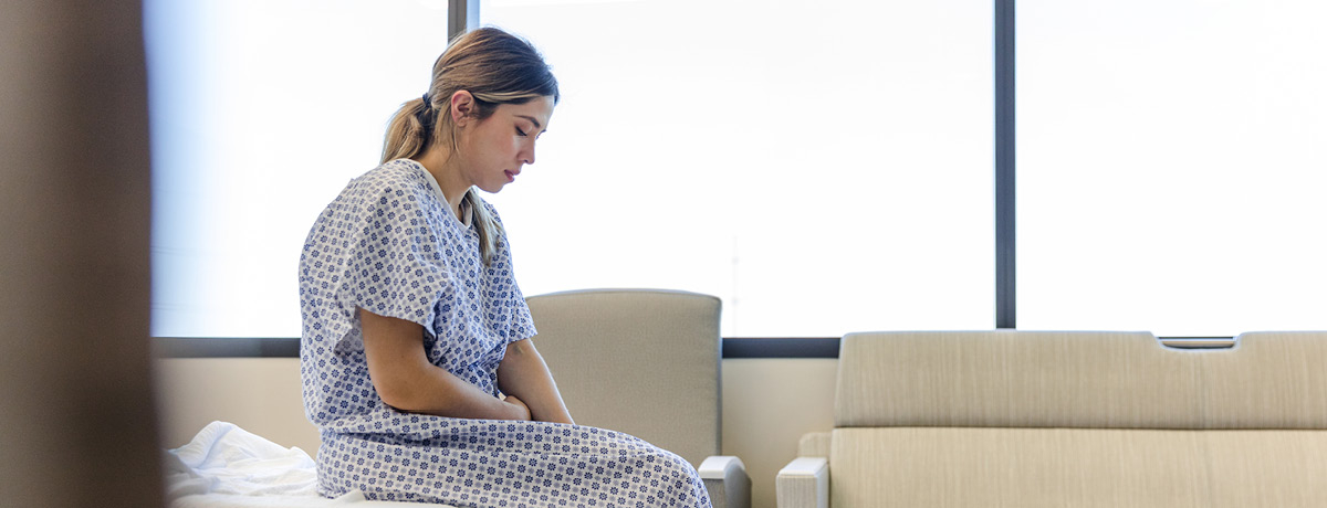 Woman in hospital gown sits on bed
