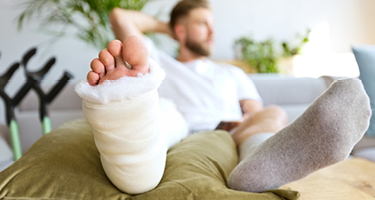 Man with cast on leg resting with crutches in background