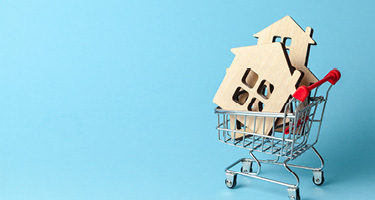 Wooden house cut outs in a shopping cart with a blue backdrop