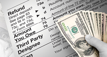 Gloved hand holding a spread of one-hundred-dollar bills near an IRS tax document 