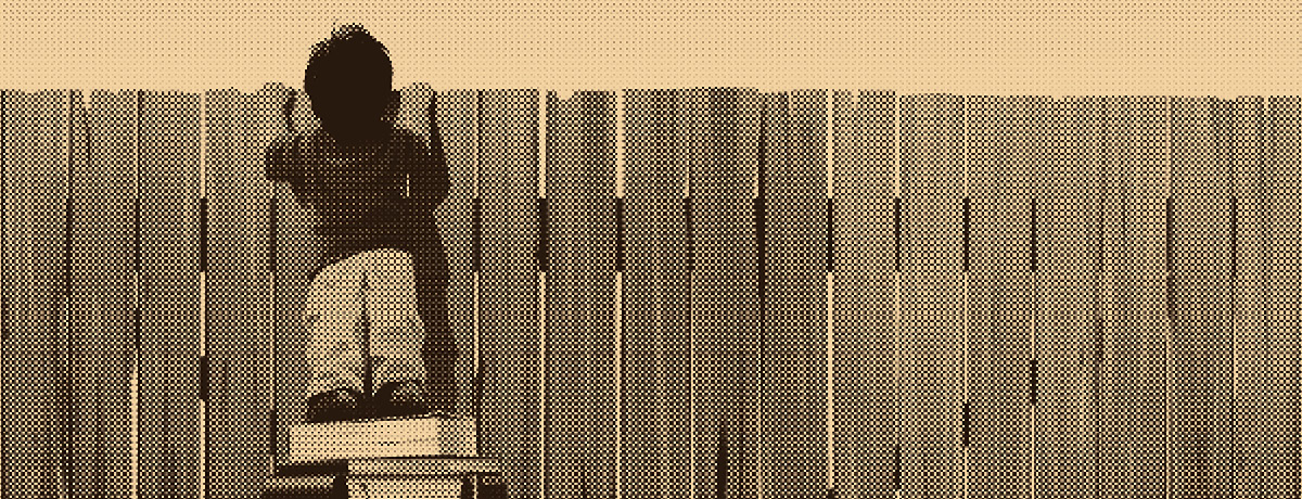 Old fashioned photo of child standing on pile of books to look over wooden fence