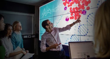 Man stares at board with red dots and DNA spirals with a group of people in the room 