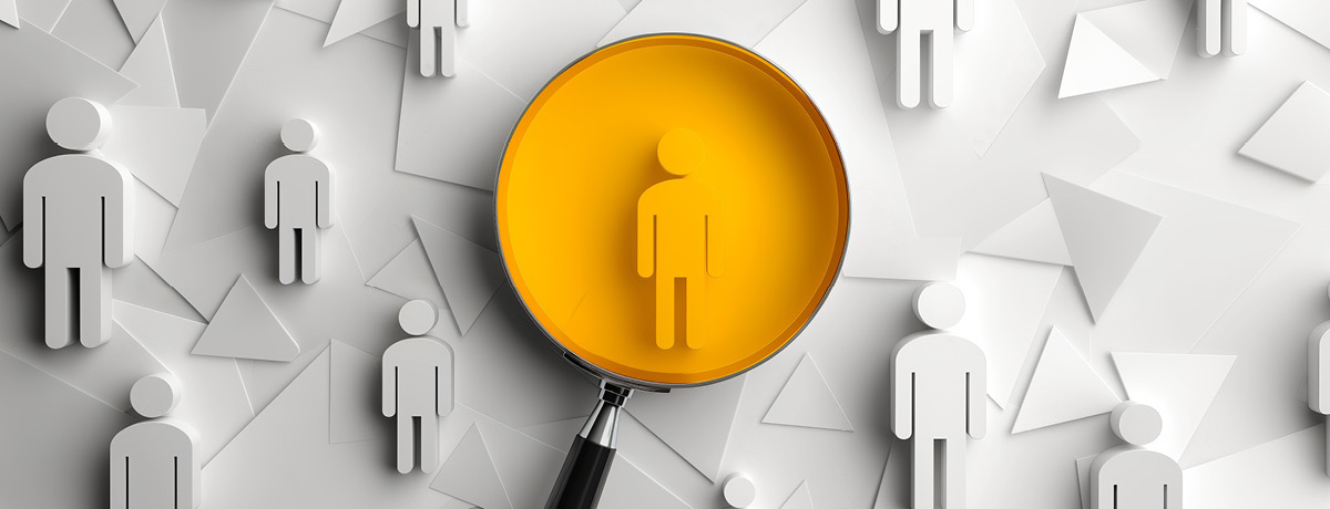 Magnifying glass focusing on a single yellow human figure among gray human cutouts.